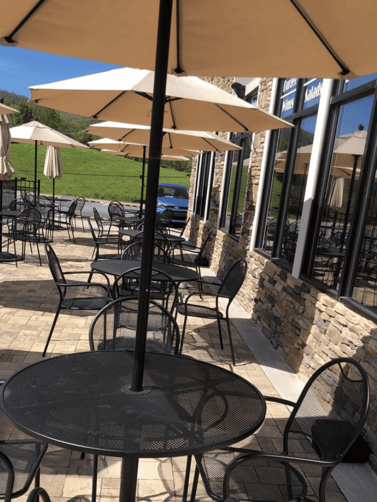 Outdoor patio dining area with tables, black metal chairs, and beige umbrellas at QuestForDirections.