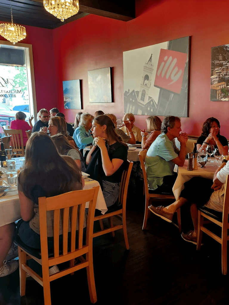 Cozy restaurant interior with groups dining, warm lighting, and vibrant red walls displaying cityscape art.