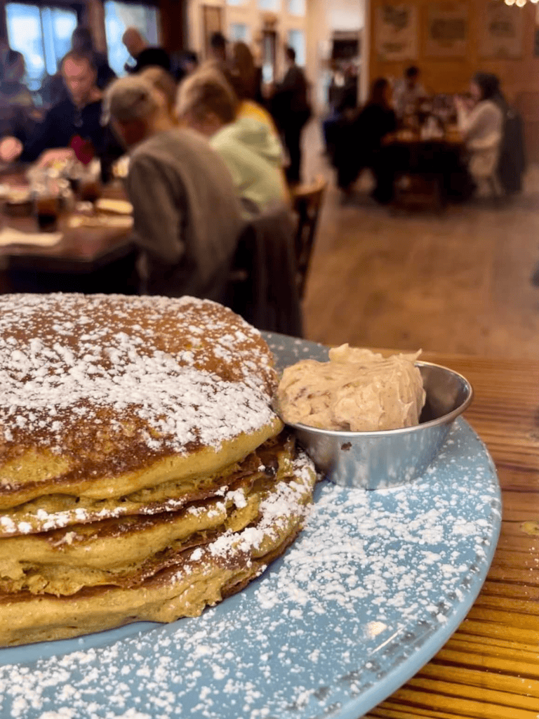 Fluffy pancakes dusted with powdered sugar served with a side of creamy butter at a cozy restaurant.