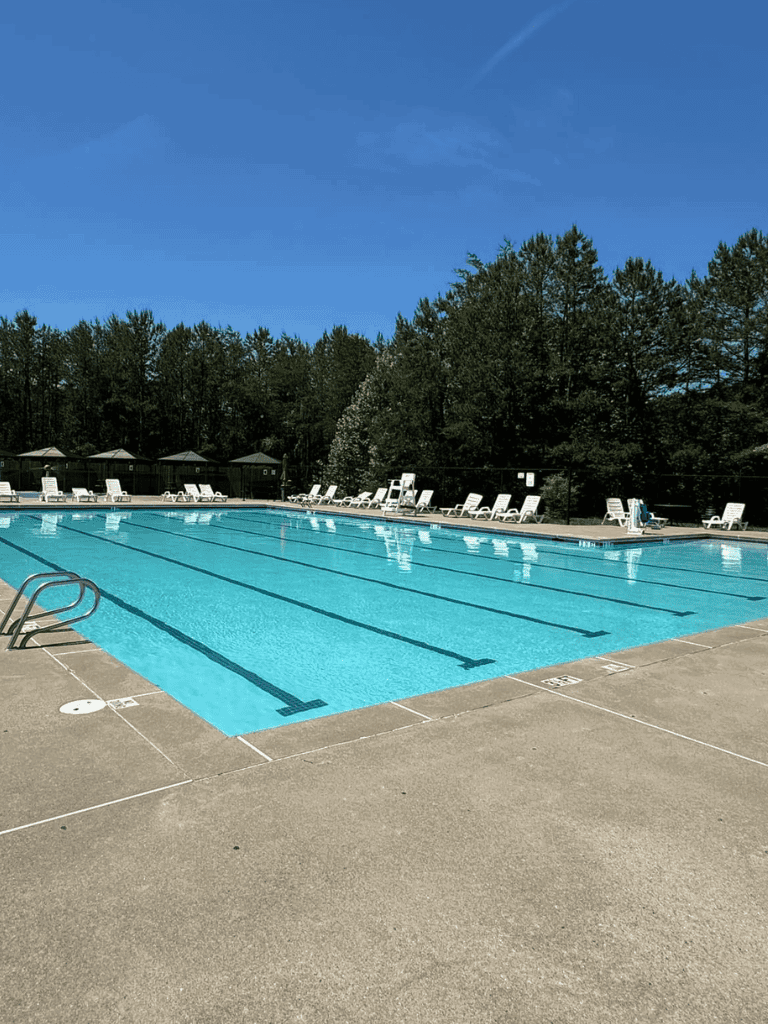 Outdoor community swimming pool with lounge chairs and surrounding trees for relaxation and recreation.