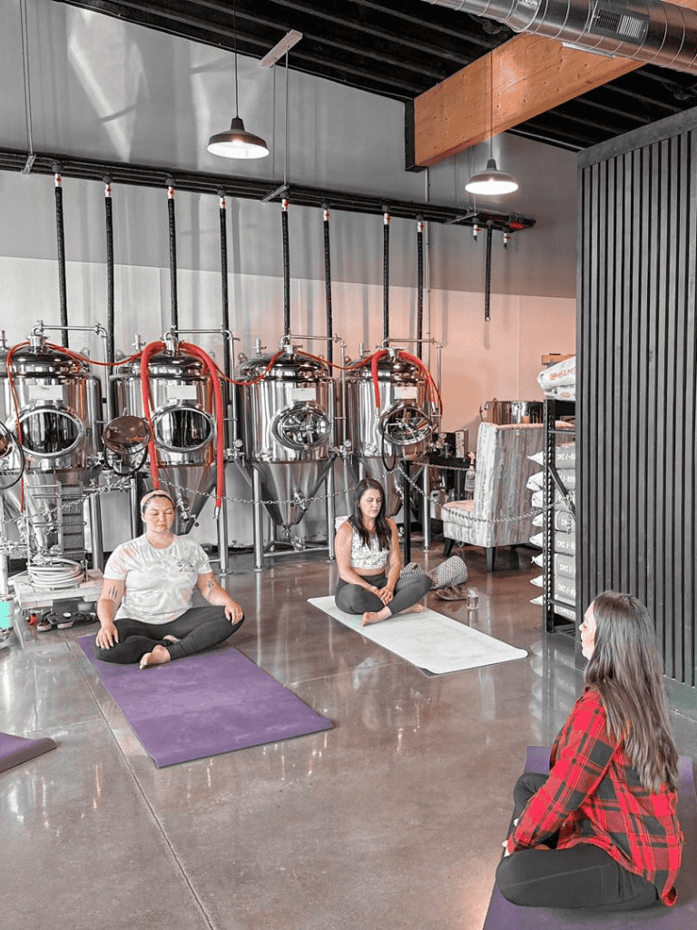 Meditation yoga class in brewery with metal brewing tanks in background.