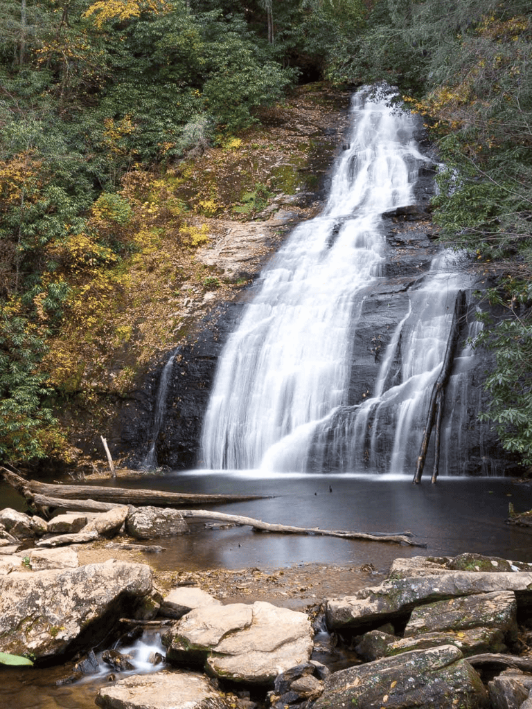 Waterfall in lush forest, scenic natural outdoor landscape, tranquil creek water, autumn foliage, peaceful nature scene.