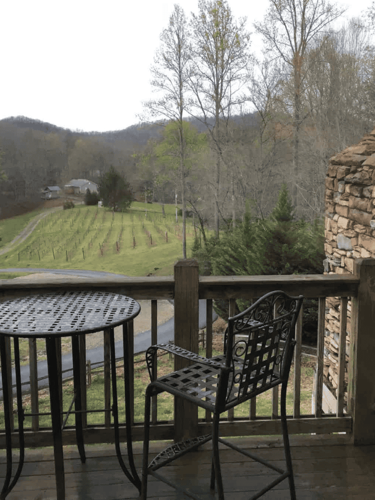 Scenic mountain view from a cozy wooden deck with outdoor seating, overlooking lush hills and countryside.