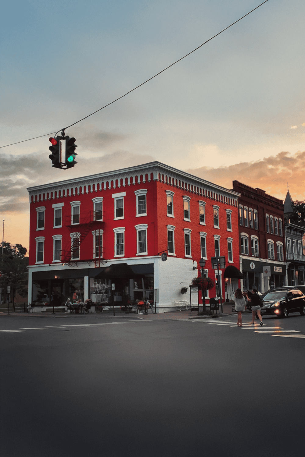 Red brick corner building with outdoor seating and traffic light at sunset.