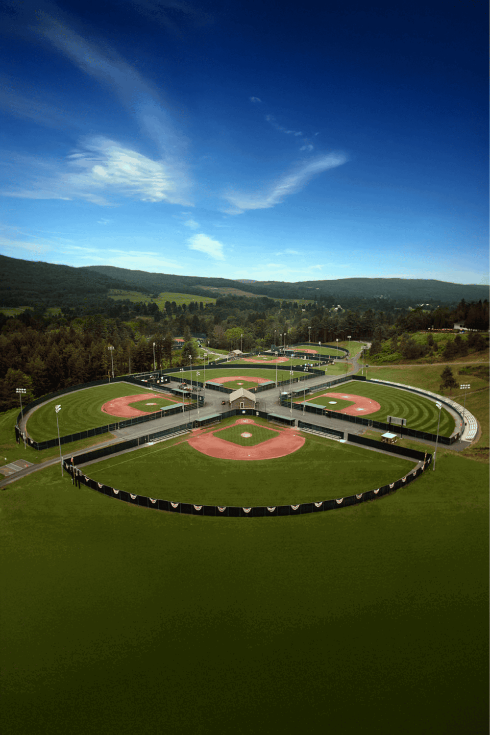 Playing field at QuestForDirections baseball complex surrounded by scenic hills and clear blue sky.