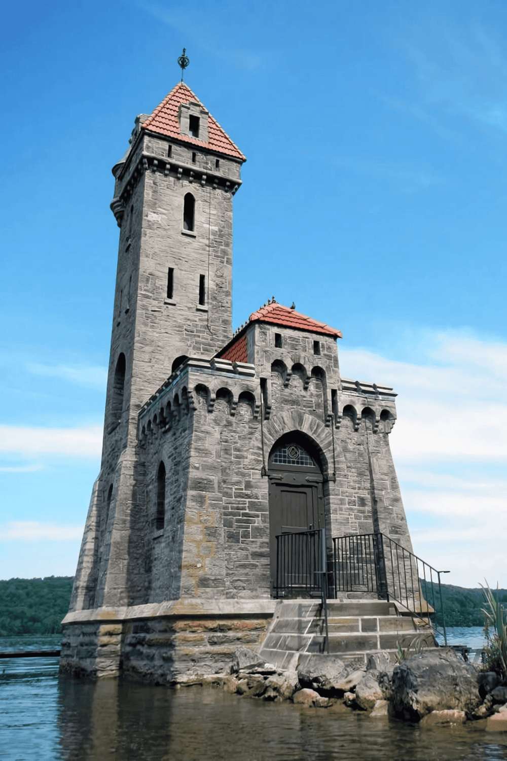 Stone castle tower by the water with a blue sky background, perfect for navigation and travel guidance.