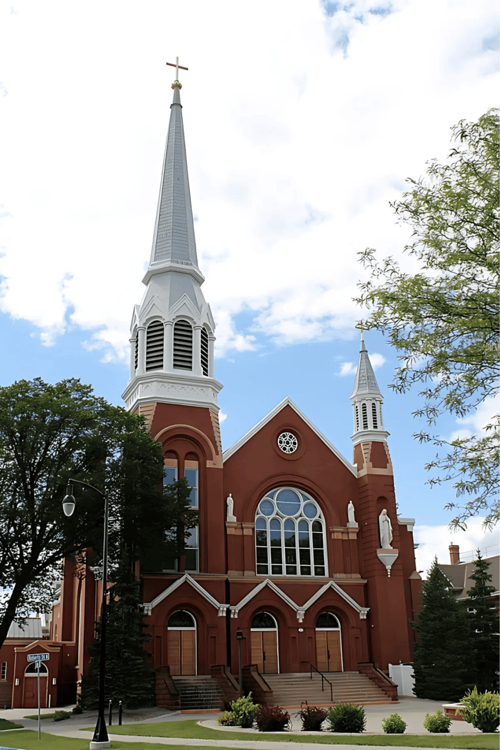 Colorful church with tall steeples and statues in front, set against a blue sky with white clouds.