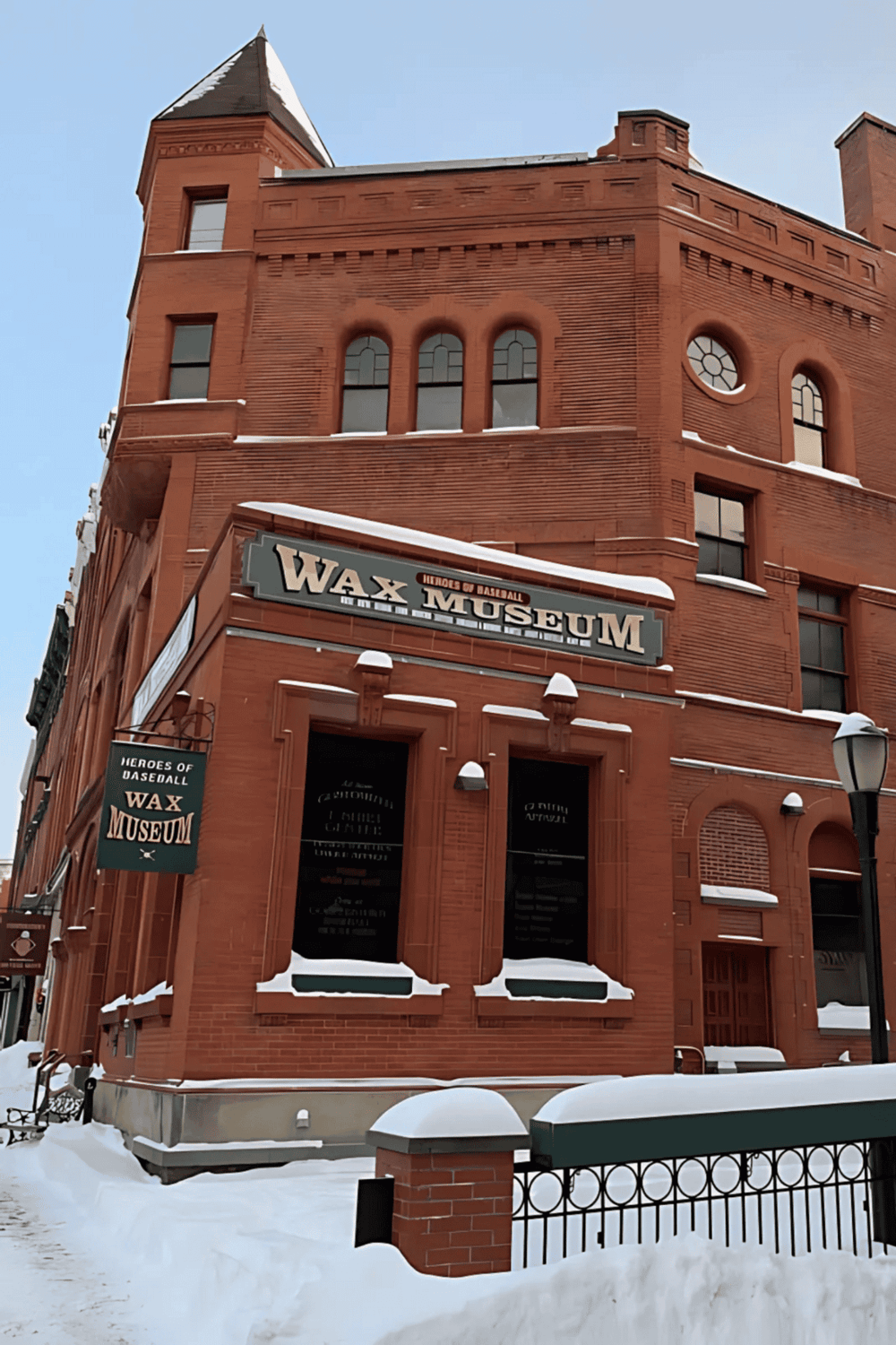 Red brick Wax Museum building with historical baseball theme, snow-covered surroundings, and vintage street lamp.