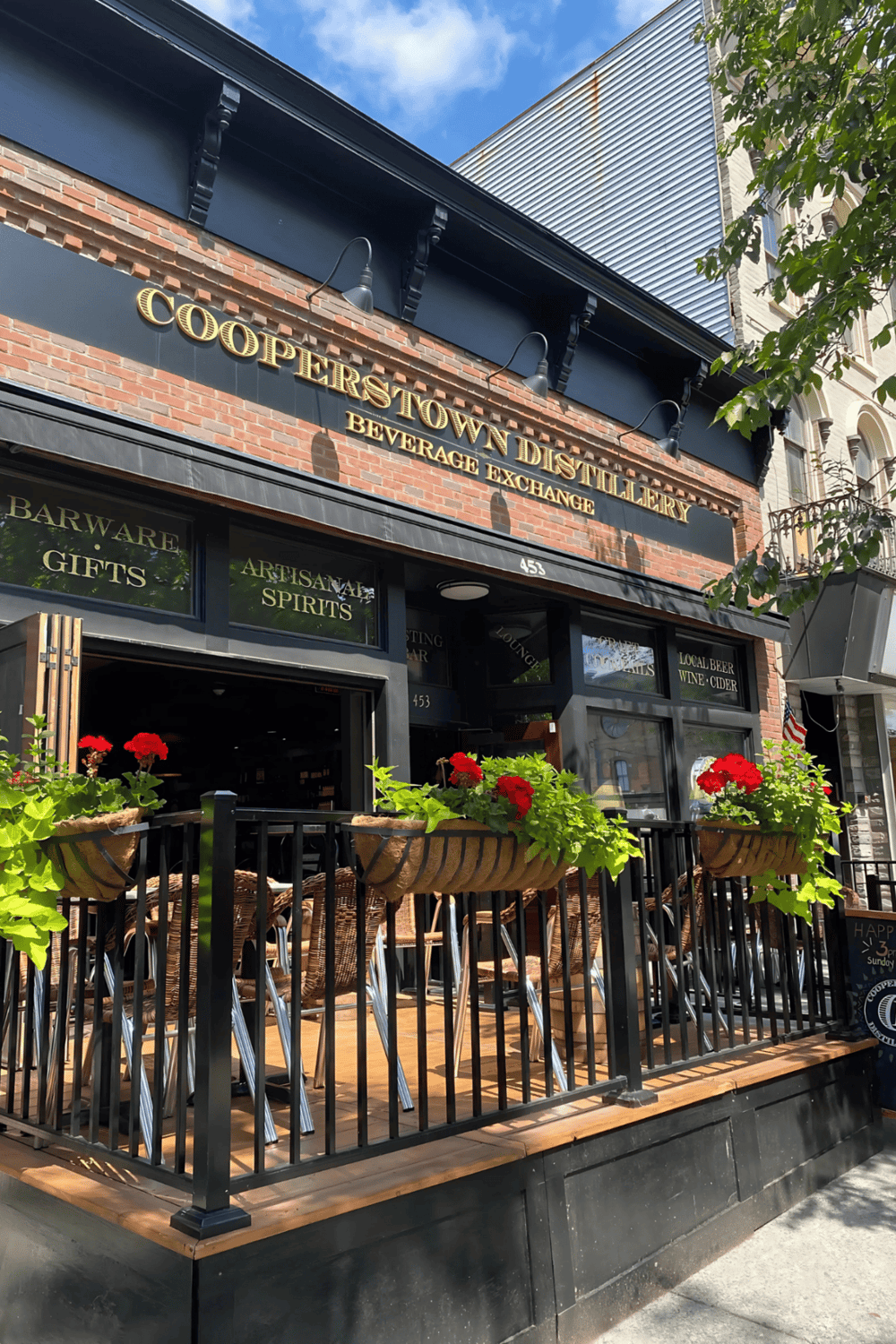 CoopersTown Distillery storefront with outdoor seating, brick facade, and floral decorations, showcasing a popular beverage exchange.