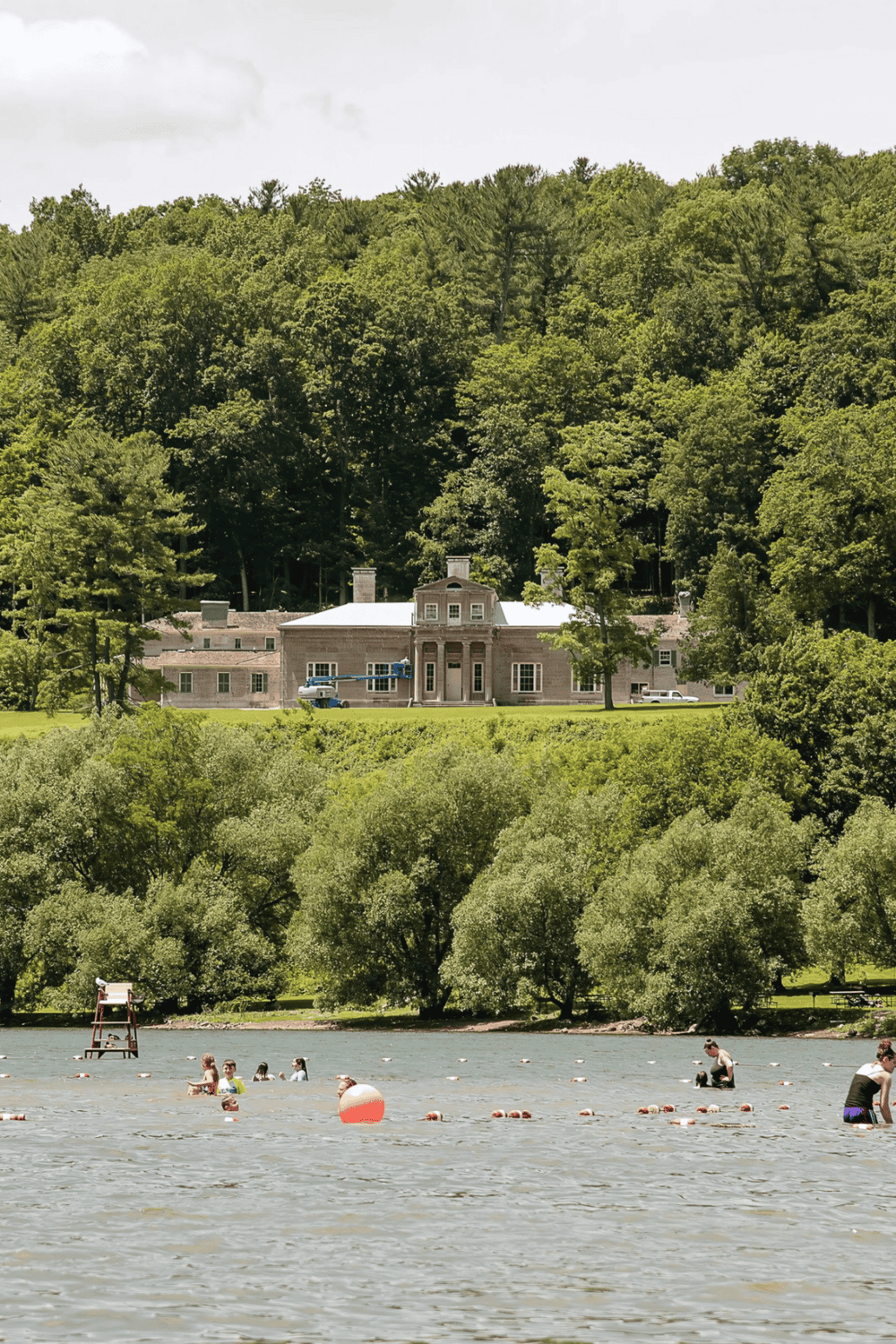 1. Elegant historical mansion nestled in lush green hills with scenic water view in foreground.