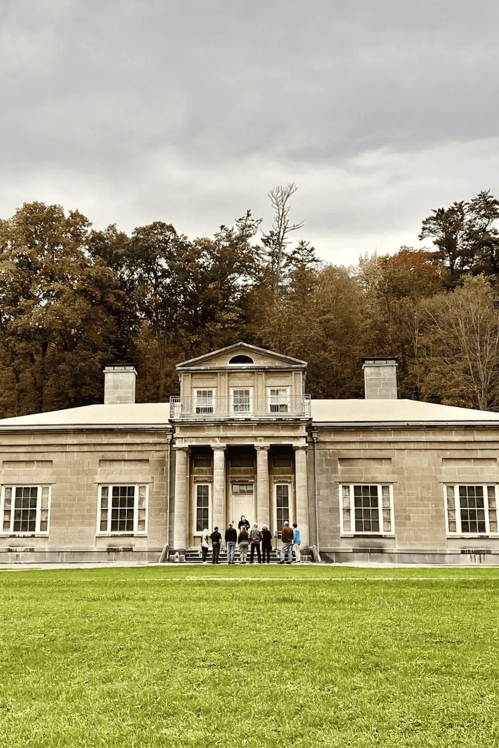 1. Historic mansion with group of visitors exploring, autumn trees in background, cloudy sky.