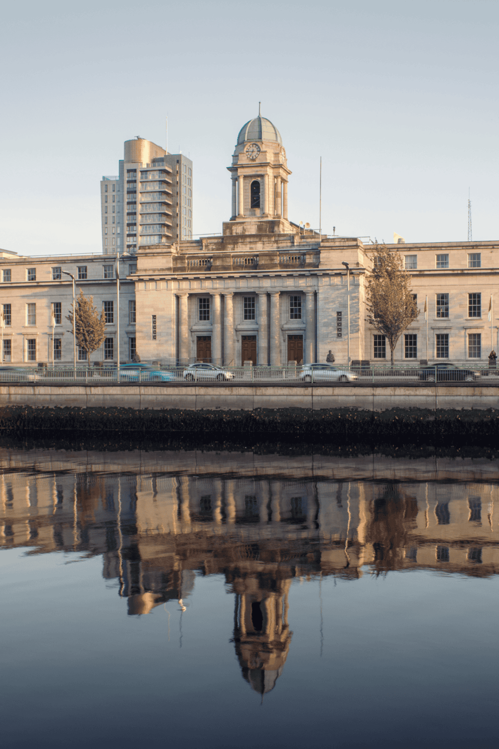 Grand historic government building reflecting on water, modern city skyline in background.