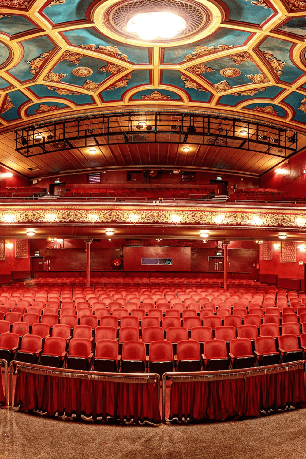 Seats inside an ornate theater with a decorated ceiling and red velvet chairs.