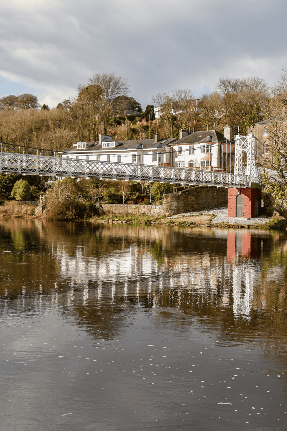 Suspension bridge over river in a scenic town setting, popular for travel and navigation.