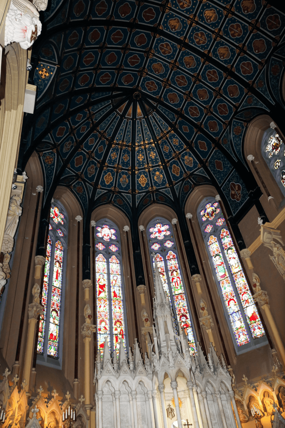 Ornate church interior with stained glass windows and intricate vaulted ceiling.