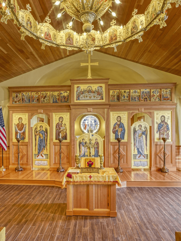 Colorful Eastern Orthodox church altar with icons and religious symbols, warm wooden interior, and ornate chandelier.