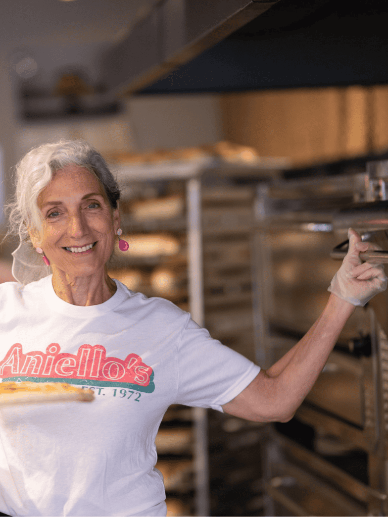 Freshly baked bread at bakery, woman smiling, bakery oven, delicious baked goods, baking success, local bakery passion, Annie's Bakery.