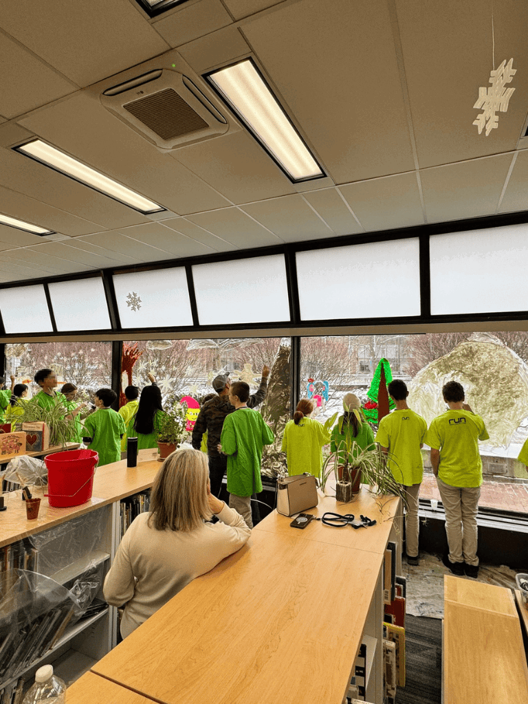 Bright classroom with children in neon green uniforms viewing winter scene outside.