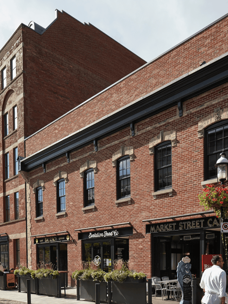 Delicate brick building with black window frames and outdoor seating area storefronts on a city street.