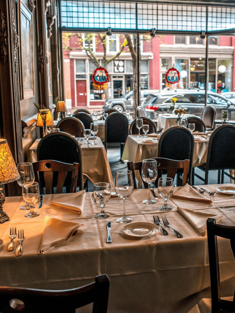 Elegant restaurant interior with table settings, large windows, and street view, perfect for dining and special occasions.