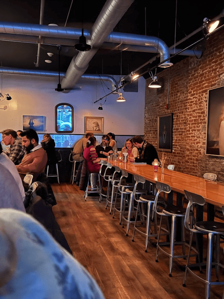 Cozy coffee shop interior with brick walls and artwork, modern industrial ceiling, people working and chatting, QuestForDirections ambiance.