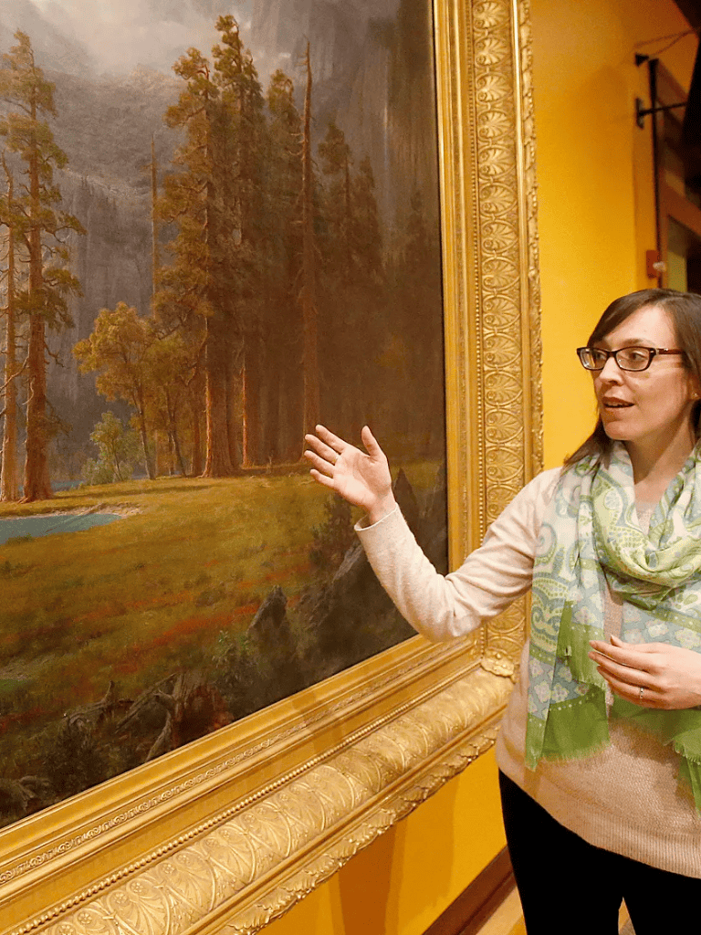 Lush forest landscape at an art gallery, person engaged with nature-inspired artwork.