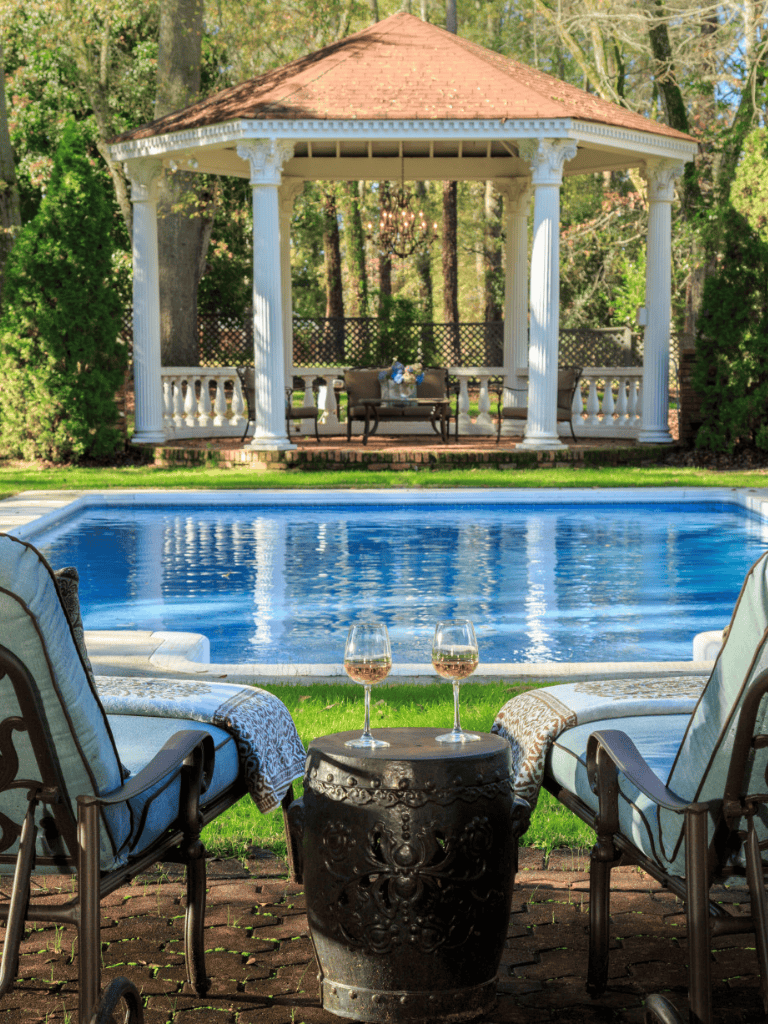 Relaxing backyard pool with gazebo, outdoor seating, and wine for perfect summer days.