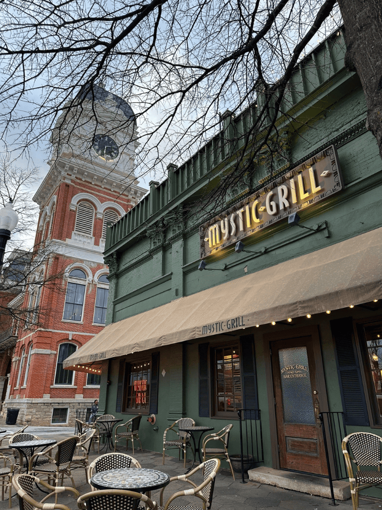 Charming outdoor seating at Mystic Grill restaurant with historic courthouse tower in background.