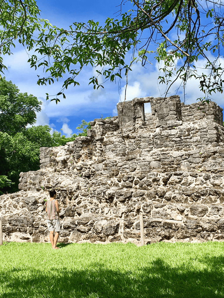 Ancient stone ruin surrounded by lush greenery and blue sky in Mexico.