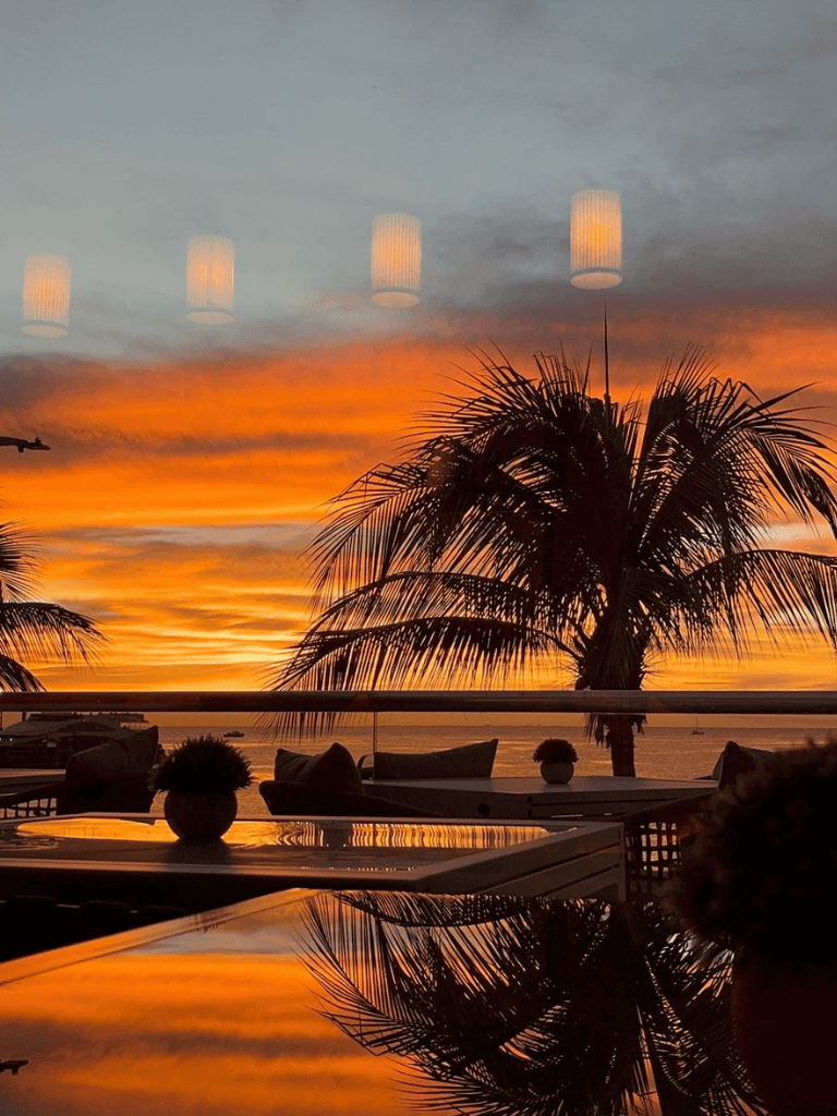 Relaxing tropical sunset at seaside restaurant with palm trees and ambient lighting.