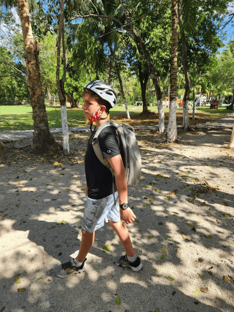Young boy with helmet and backpack walking outdoors through tropical park — perfect for adventure, exploration, and outdoor activities.