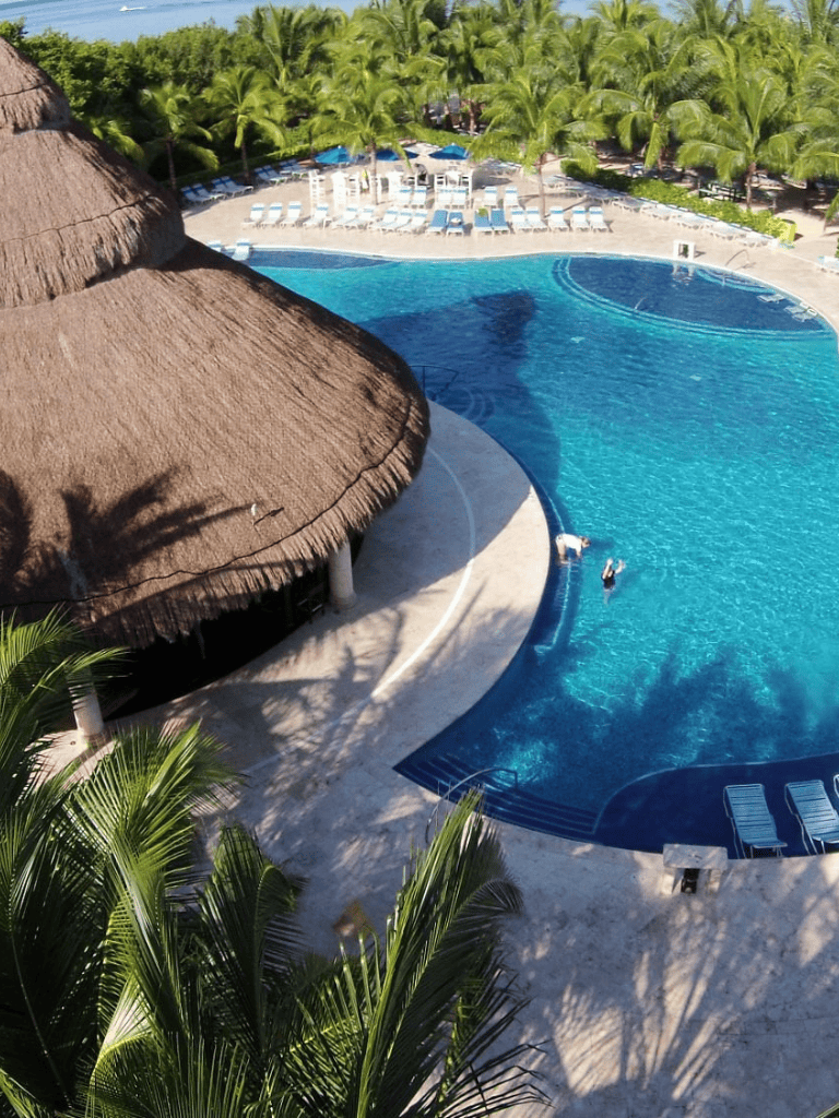 Luxurious resort pool with tropical palm trees and thatched roof cabanas, perfect for relaxing vacations.