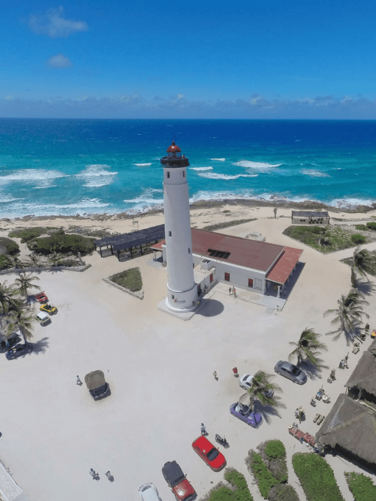 Seaside lighthouse on sandy beach with ocean view and clear blue sky.
