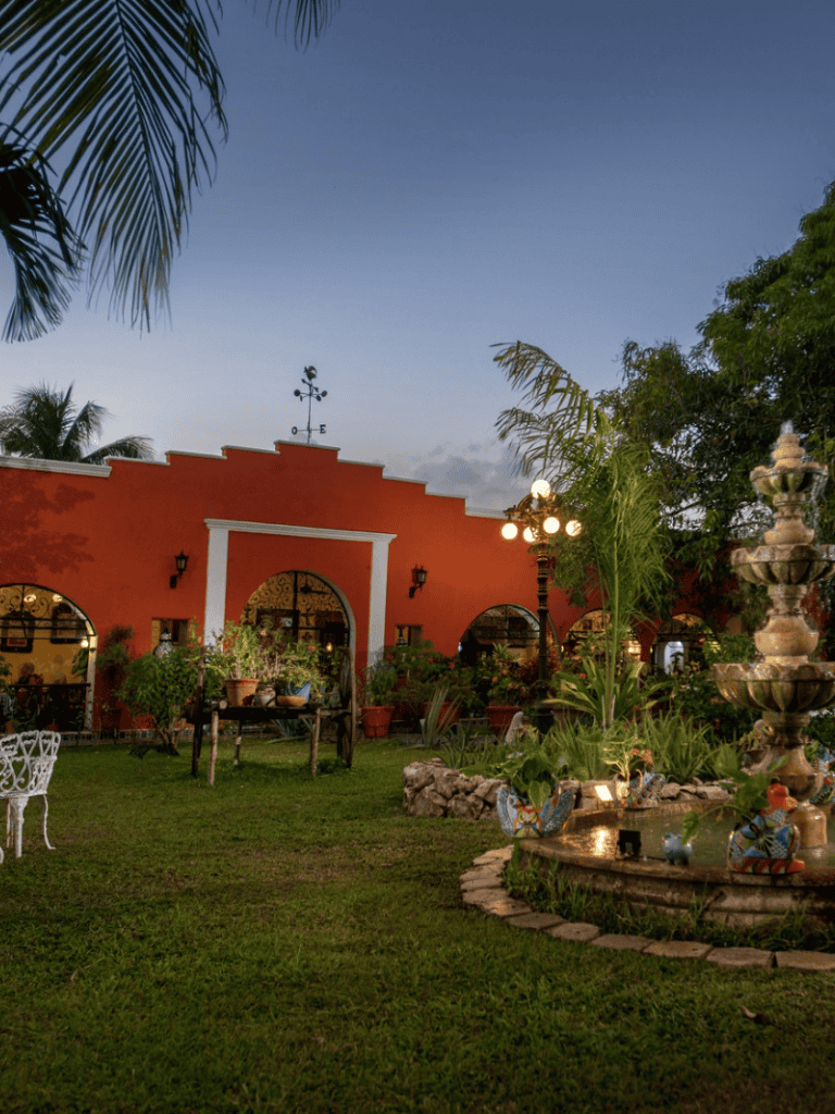 Charming outdoor patio with lush garden and vibrant red building, perfect for dining and relaxation.