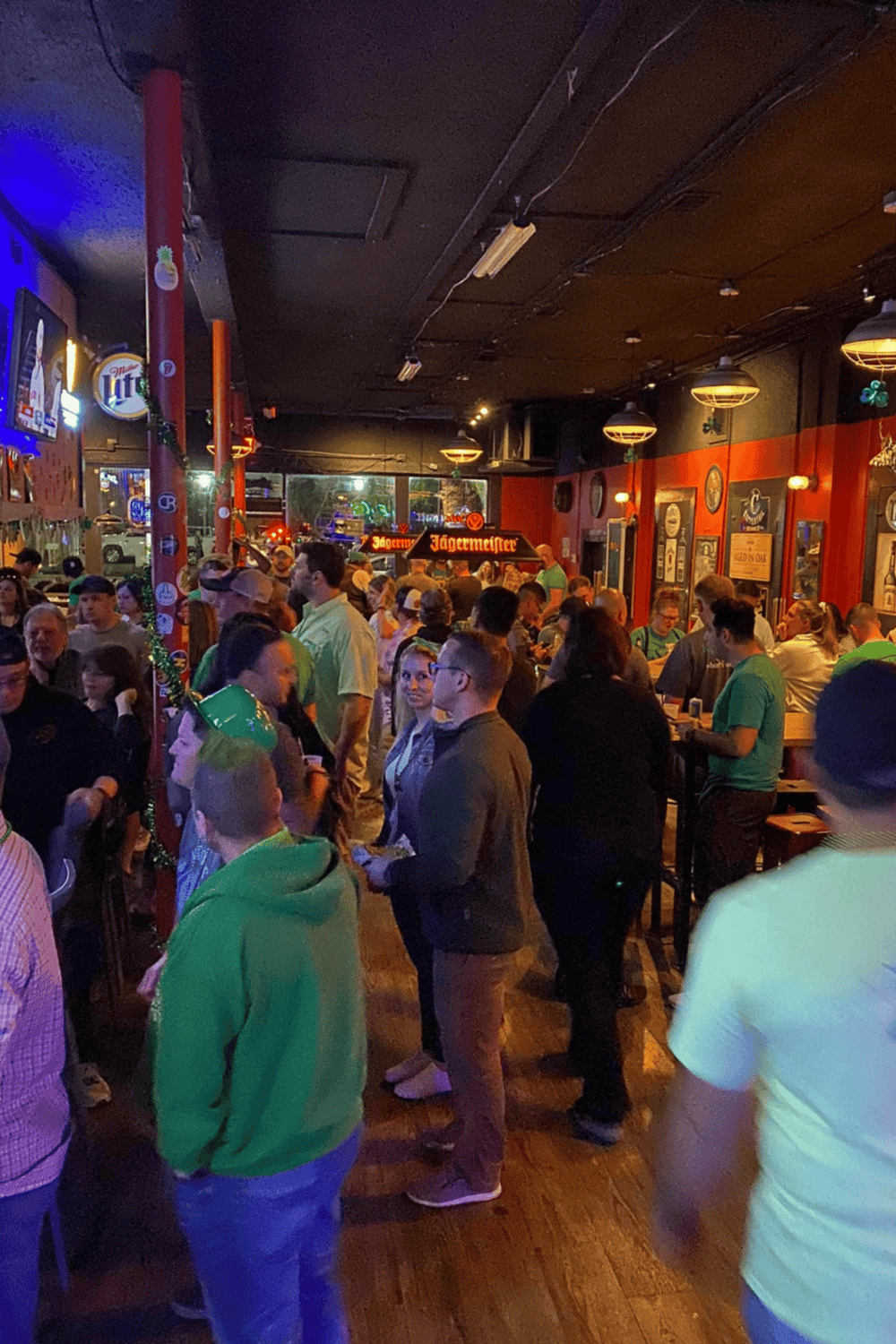 Crowded bar scene with people enjoying drinks, lively atmosphere, and sports memorabilia decor.