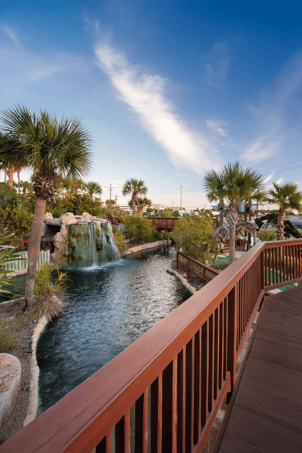 Lush tropical landscape with waterfalls, palm trees, and wooden walkways, ideal for family fun and outdoor activities.