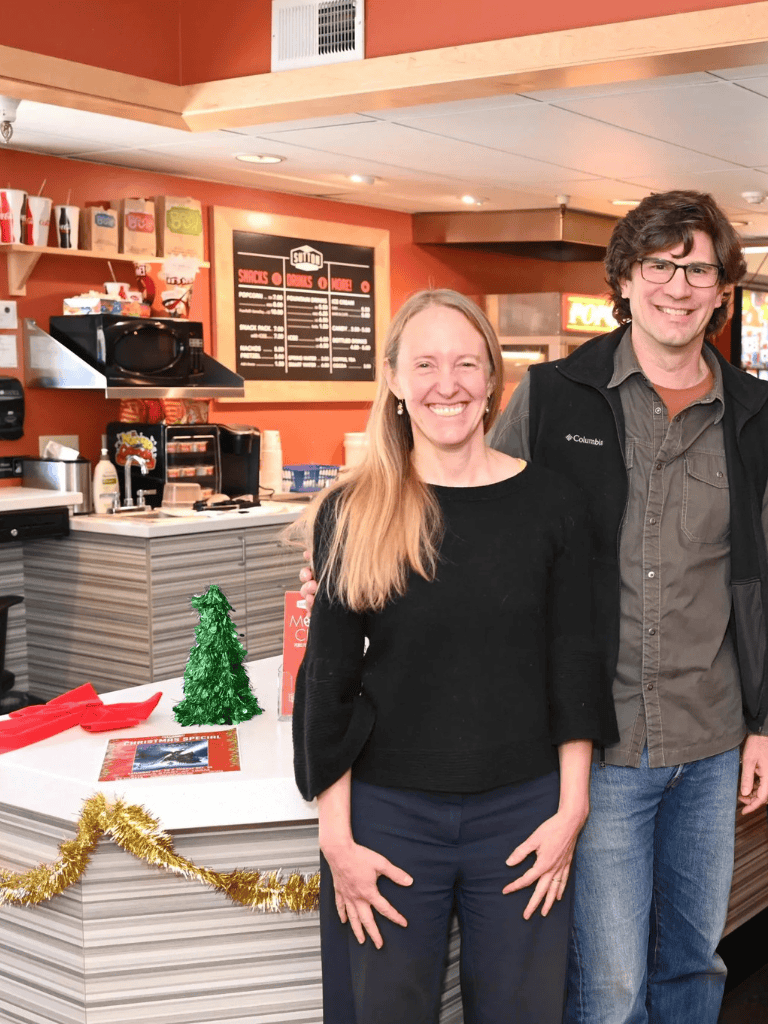 A woman smiling at a counter decorated with Christmas ornaments and two people in a casual dining restaurant.