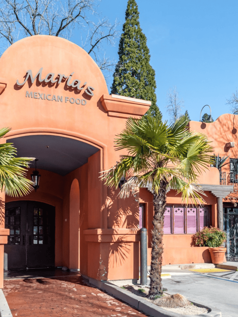 Charming Mexican restaurant with pastel-colored exterior, palm trees, and vibrant atmosphere.