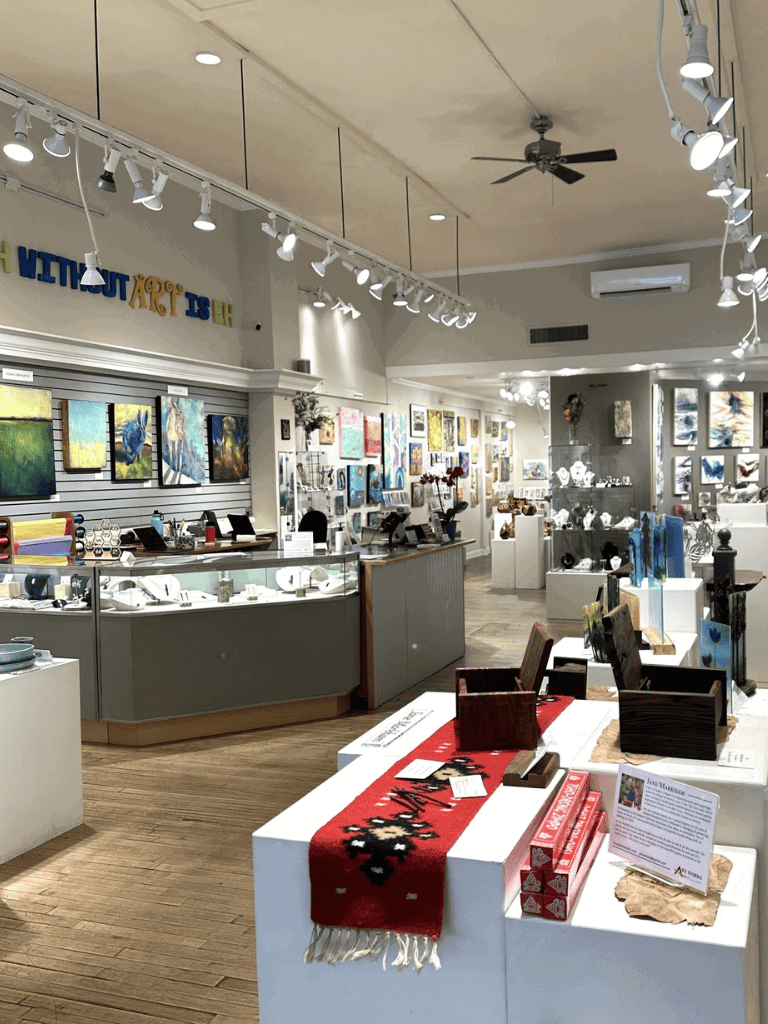 Bright art and gift shop interior showcasing paintings, jewelry, and artisanal products for sale.
