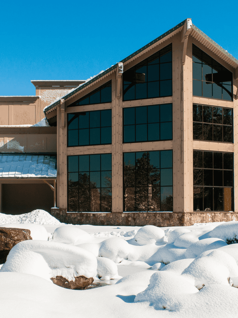 Modern mountain lodge with large glass windows and snow-covered landscape in winter.