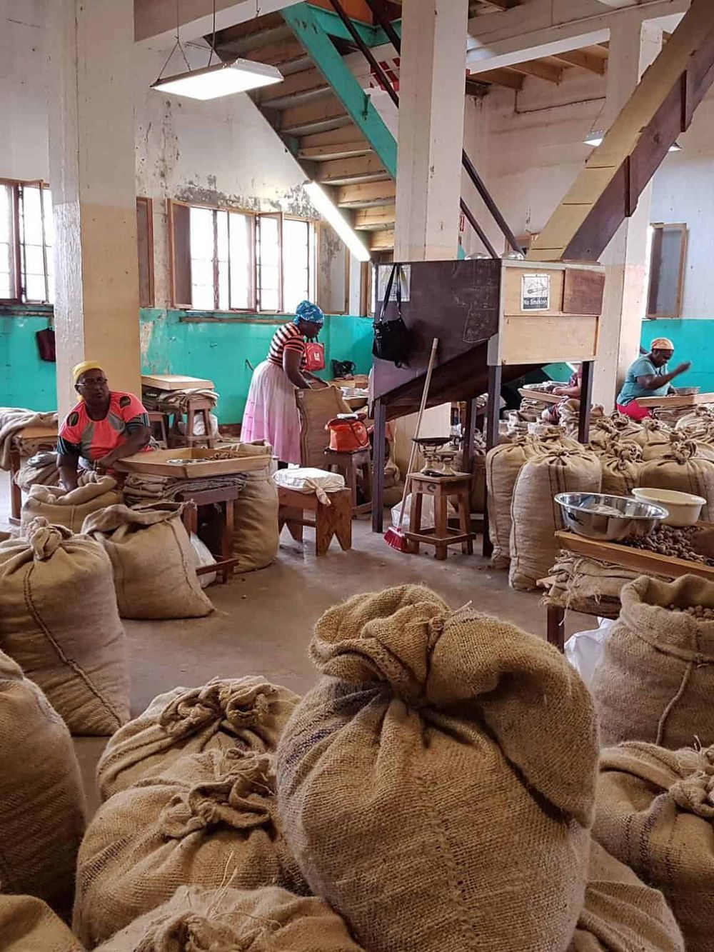 Bags of coffee beans in a rustic warehouse with workers sorting and handling coffee products.
