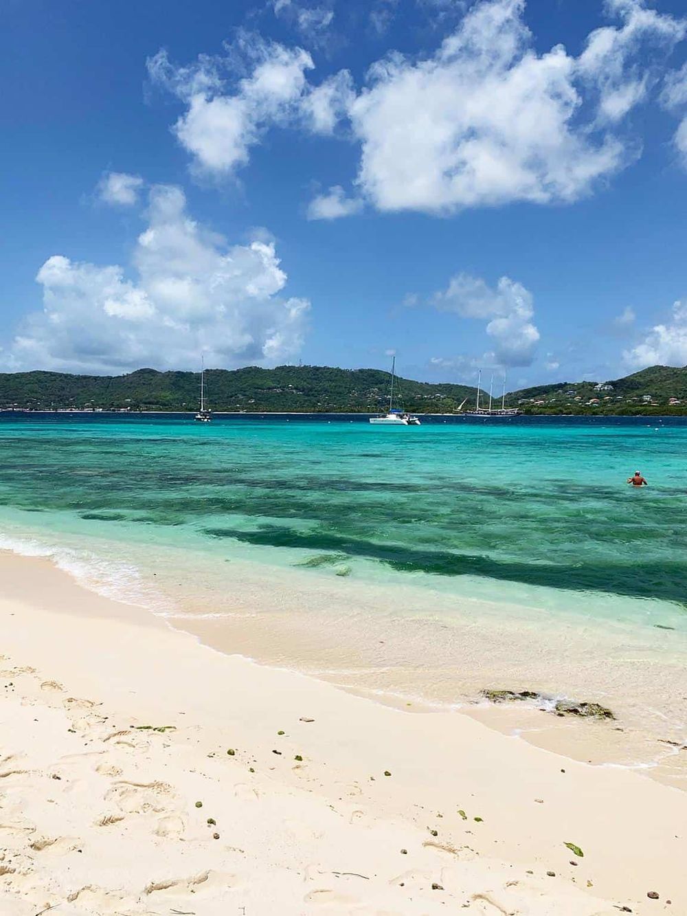 Stunning Caribbean beach scene with turquoise waters, white sand, and sailboats under a bright blue sky.