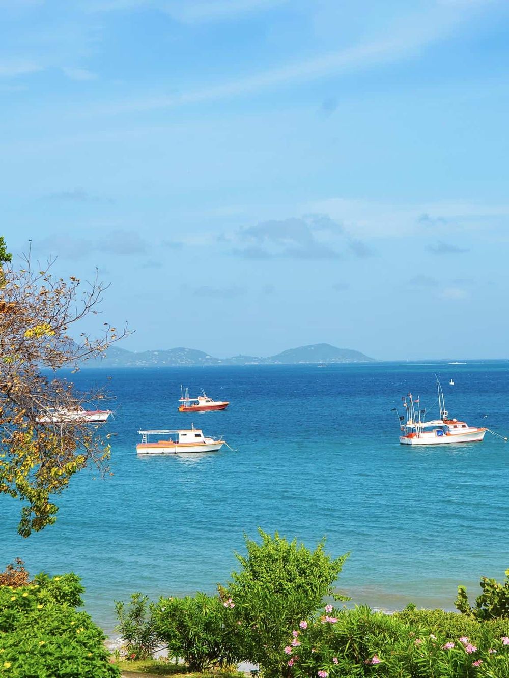 Serene ocean view with boats, lush greenery, and distant islands on a sunny day.
