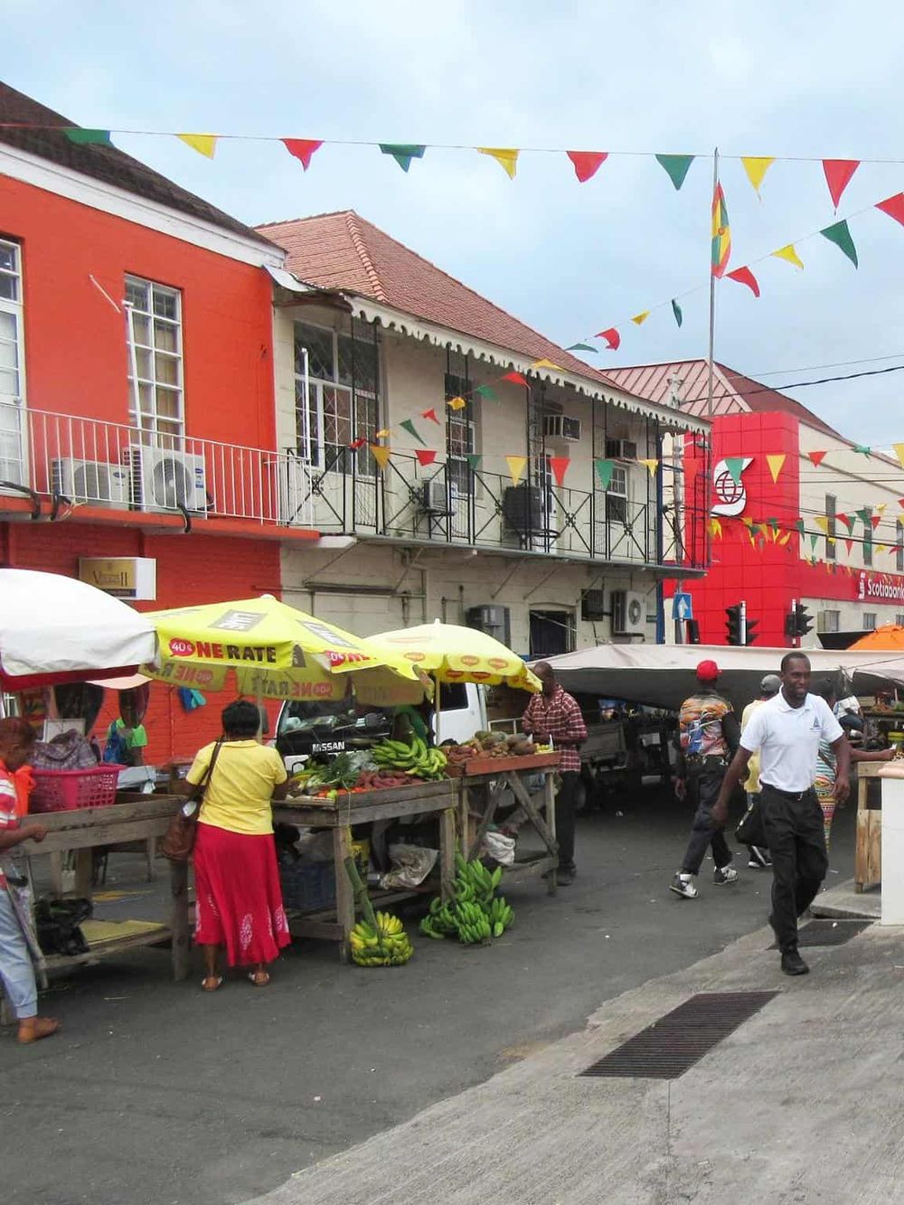 Colorful street market with vendors and fresh produce in front of vibrant buildings.