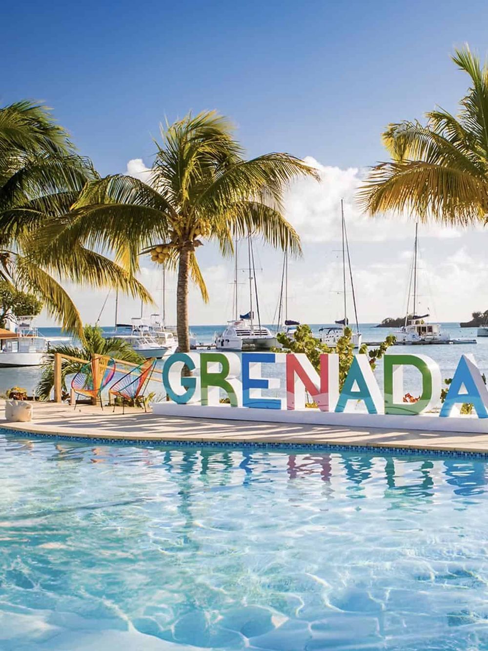 Bright tropical scene with palm trees, yachts, and colorful Grenada sign by the poolside.