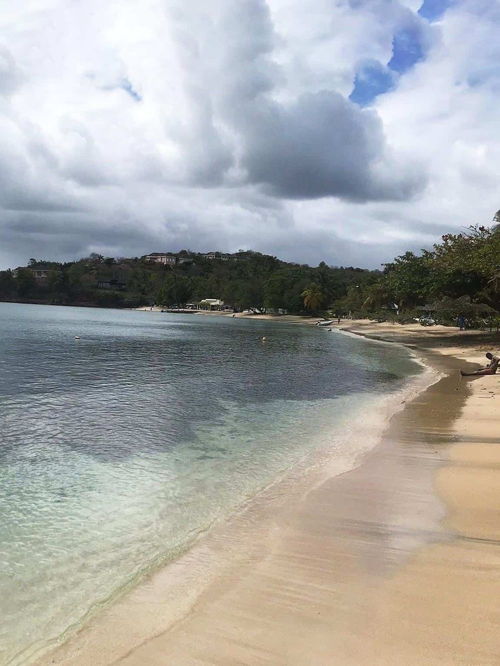 Tranquil beach scene with clear waters, cloudy sky, and lush greenery, perfect for travel and adventure.