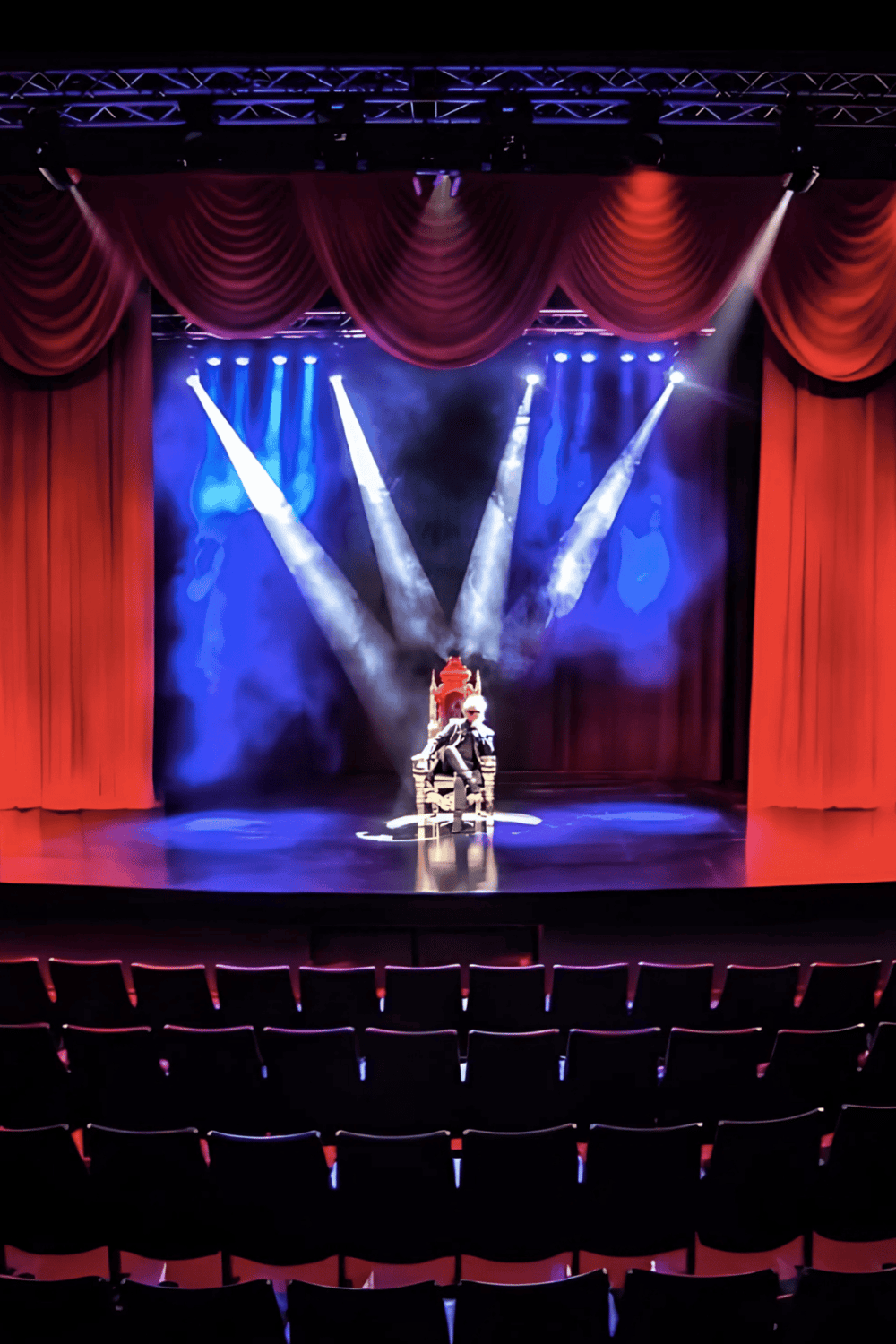 Performer on stage with dramatic lighting and red curtains, capturing live entertainment and theater performances.