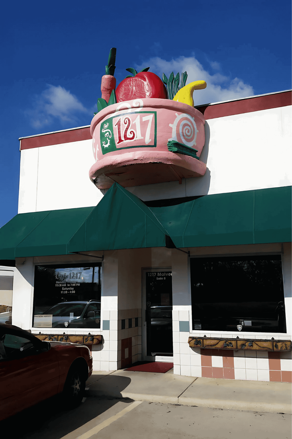 Ice cream shop sign with colorful toppings and clear store hours, located on a busy street.