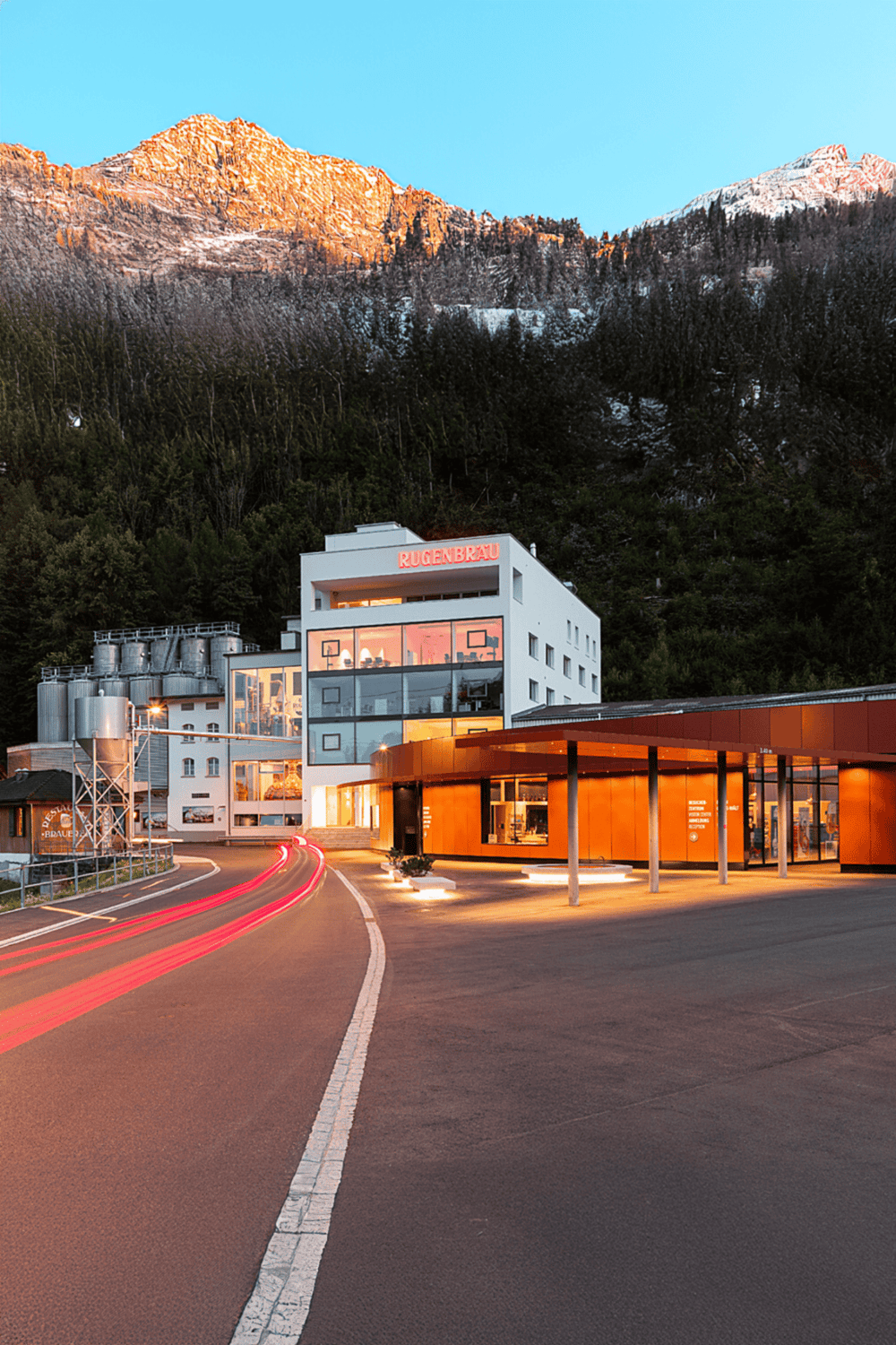 Modern brewery building in a scenic mountain village with a mountain backdrop at sunset.