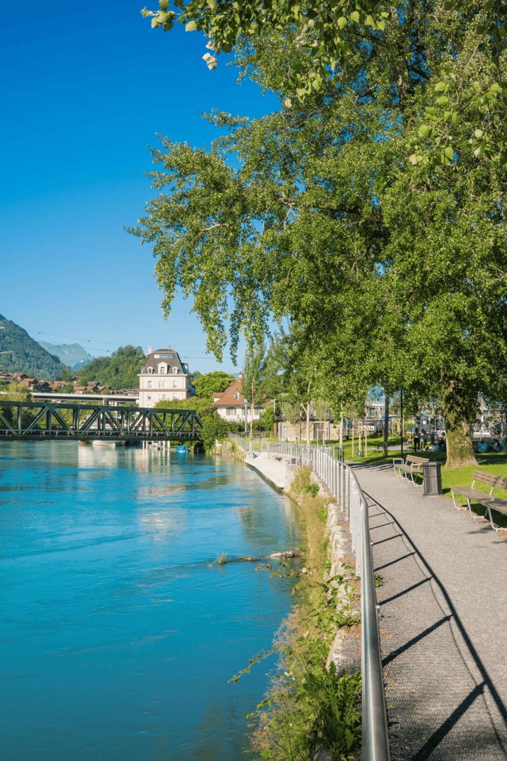 Serene riverwalk with lush trees and scenic mountain views in a charming town.